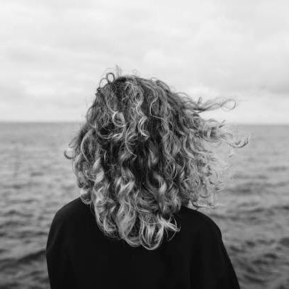 a person with long curly hair standing in front of water, fertilitet